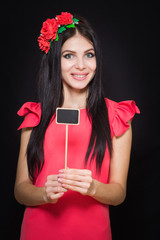 Beautiful woman with a wreath of red flowers holds a wooden plaque. Close-up