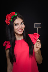 Beautiful woman with a wreath of red flowers holds a wooden plaque. Close-up