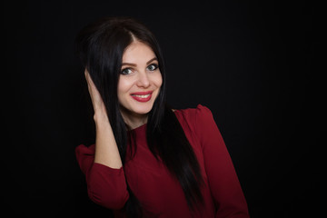 Beautiful brunette woman with blue eyes on a dark background holds her hair. Close-up. Space for text