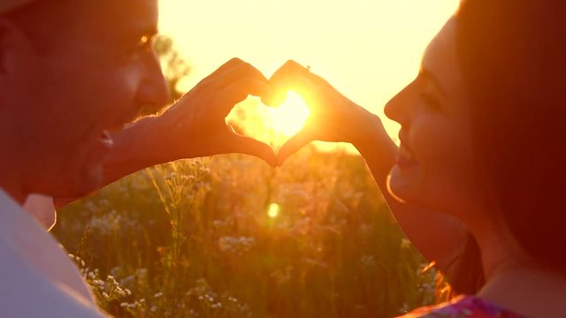 Beauty girl and her handsome boyfriend making shape of heart by their hands against beautiful sunset on horizon