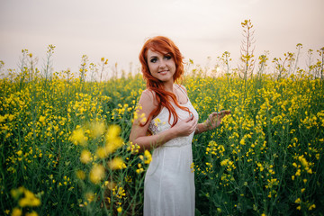 Fototapeta premium Young red-haired woman in a rapeseed field
