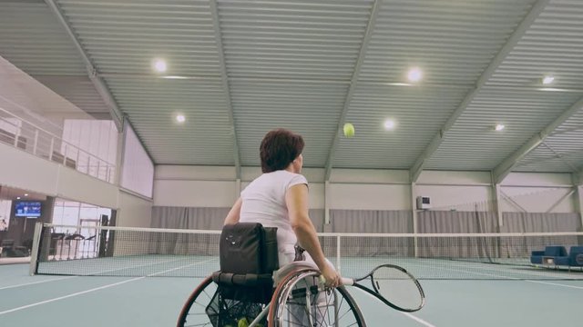 Disabled mature woman on wheelchair playing tennis on tennis court.