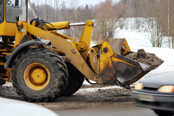 Excavator cleans the road in the city of dirty snow.