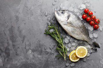 Fresh dorado or gilthead bream cooking with rosemary, cherry tomatoes and lemon on stone background