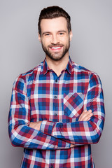 A portrait of young confident handsome smiling guy in checkered shirt with crossed hands standing...