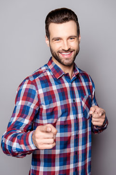 A close up portrait of young smiling man standing against gray background and pointing at you with his fingers