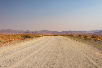 Obraz premium Gravel 4x4 road crossing the colorful desert at Twyfelfontein, in the majestic Damaraland Brandberg, scenic travel destination in Namibia, Africa.