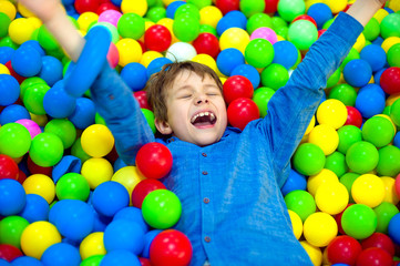 Fototapeta na wymiar Happy little kid boy playing at colorful plastic balls playground high view. Funny child having fun indoors.