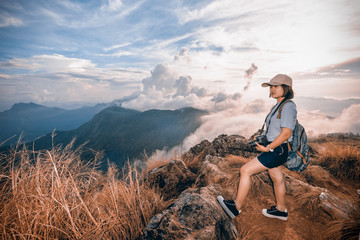 Vintage style hiker young woman happy with camera and backpack looking beautiful landscape nature of mountain in Phu Chi Fa Forest Park, Chiang Rai, Thailand, on Sienna-Blue color two tone