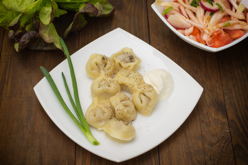 Russian pelmeni with fresh green onion on plate. Wooden background. Top view. Close-up