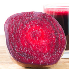 Cut half beetroot and fresh beet juice in glass on wooden table, white background.