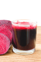 Fresh beet juice in glass and sliced beetroot on wooden table, white background.