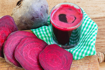 Fresh beet juice in glass and sliced beetroot on wooden board with napkin.