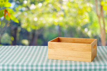 Empty wooden box on table with green scott pattern tablecloth over blur tree with bokeh light background, product display montage