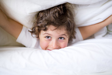 Adorable little boy in white t-shit lying in bed