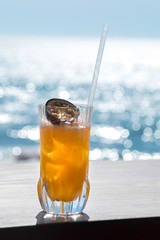 A glass filled with cold orange juice with ice on the beach
