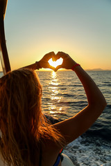 Young blonde female making heart shape with hands by the sea on a sunny day