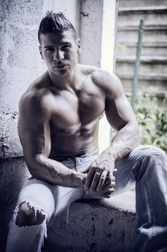Muscular young latino man shirtless in jeans sitting against concrete wall  looking at camera Stock Photo | Adobe Stock