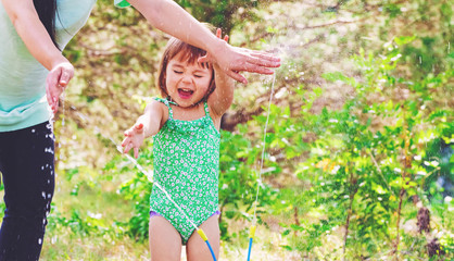 Toddler girl playing in a sprinkler with her mother