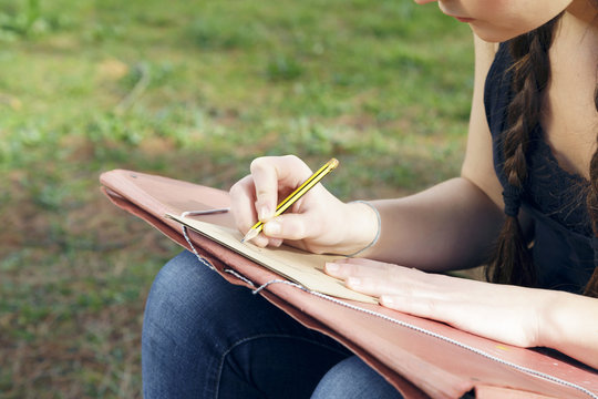 Young brunette woman artist, drawing sketch and thinking, looking for inspiration. Outdoors, in nature.