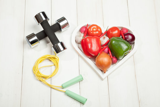 Sport and diet. Healthy lifestyle. Vegetables, dumbbells. Peppers, tomatoes, garlic, onion  radish in a heart on  white background
