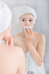 woman looking mirror and cleaning her face with cotton