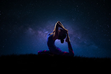Silhouette of a woman practicing yoga with milky way night sky in background