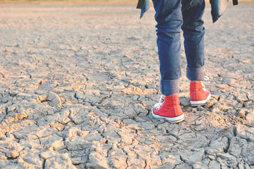 Fototapeta premium Feet sneaker on crack dry ground, concept drought