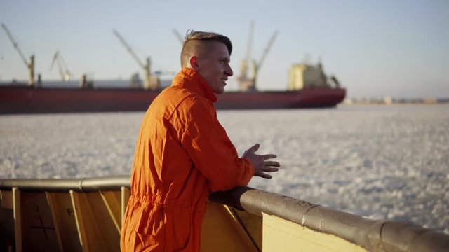 Young man in orange uniform traveling on board of the ship in winter.