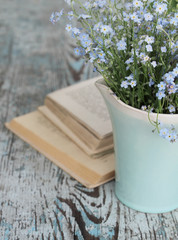 Blue jug with bouquet of forget-me-nots on wooden table and the opened book