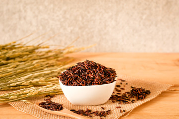 the brown raw rice in bowl with  dried rice plant on wooden table background.