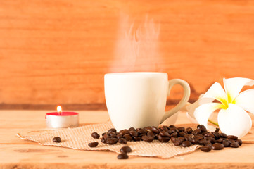 the hot coffee in the white cup on wooden table with coffee seed and red candle