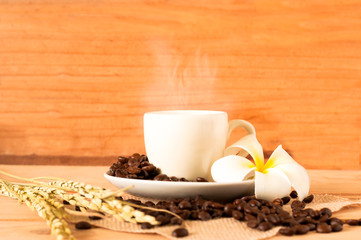 the hot coffee in the white cup on wooden table with coffee bean seed