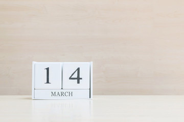 Closeup surface white wooden calendar with black 14 march word on blurred brown wood desk and wood wall textured background with copy space , selective focus at the calendar