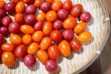 Ripe cherry tomatoes with water droplets in bamboo sieve.
