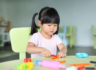 Child girl sitting at the table and plays artificial fruit.