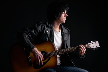 Obraz na płótnie Canvas Rockstar in biker leather jacket playing solo on acoustic guitar.