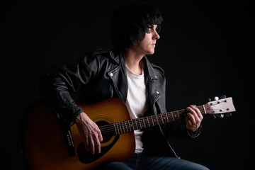 Obraz premium Rockstar in biker leather jacket playing solo on acoustic guitar.