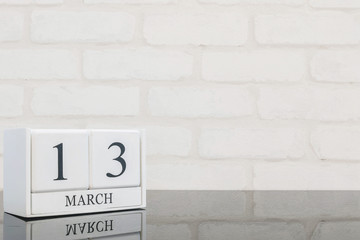 Closeup white wooden calendar with black 13 march word on black glass table and white brick wall textured background with copy space , selective focus at the calendar
