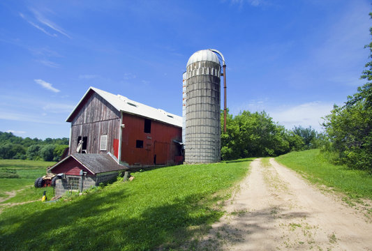 Agricultural background. Summer countryside landscape with old farm buildings and rural road at sunny summer day. Midwest USA, Wisconsin.