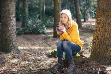 Hiker woman drinking from mug in forest. 