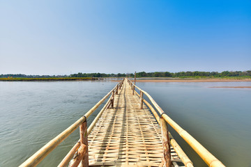 Fototapeta na wymiar beautiful long bamboo bridge on river with blue sky at sunny day. soft focus