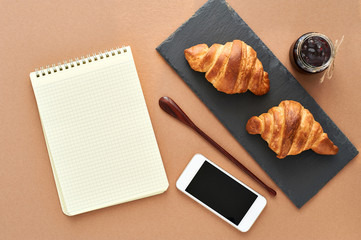 Business breakfast of two French croissants with notepad and smartphone