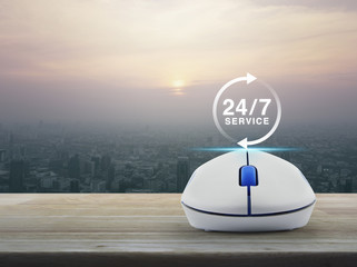 24 hours service icon with wireless computer mouse on wooden table over modern city tower at sunset, vintage style, Full time service concept