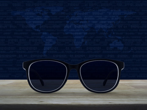 Black eye glasses on wooden table over world map and computer binary code blue background, Business vision concept, Elements of this image furnished by NASA