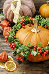 Pumpkin decorated with wreath with red berries (cotoneaster horizontalis) and green moss.