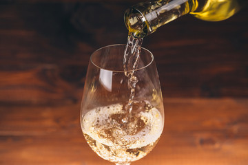 Pouring white wine from a bottle in a close up view of the wineglasses against wooden background © Ievgenii Meyer