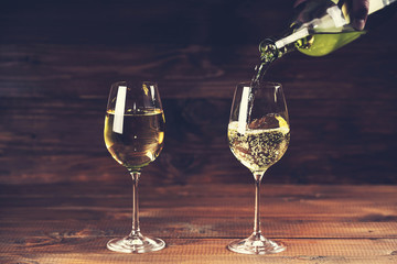Pouring white wine from a bottle in a close up view of the wineglasses against wooden background