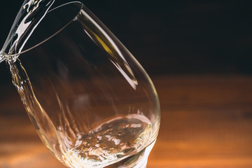 Pouring white wine from a bottle in a close up view of the wineglasses against wooden background