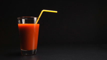 Tomato juice in a glass with a tube on black background